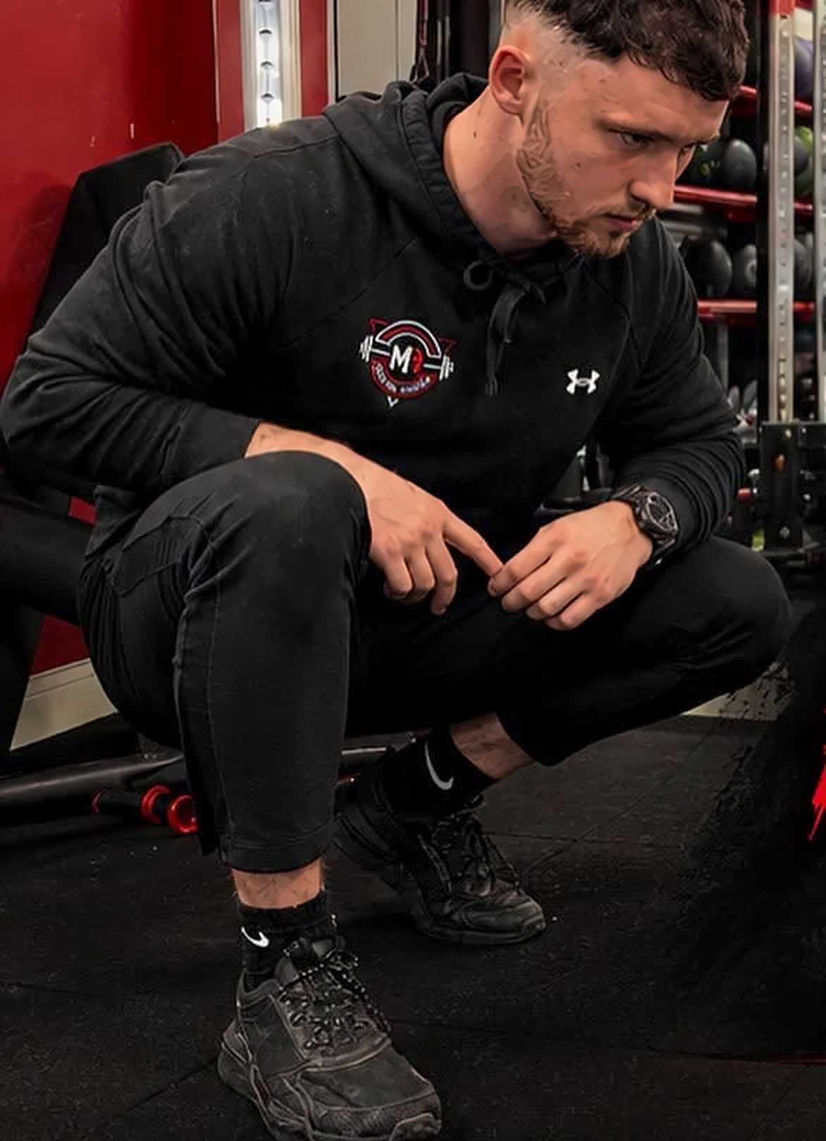 Michael Roach, coach at MR Personal Training, crouched on the gym floor in an MR hoodie